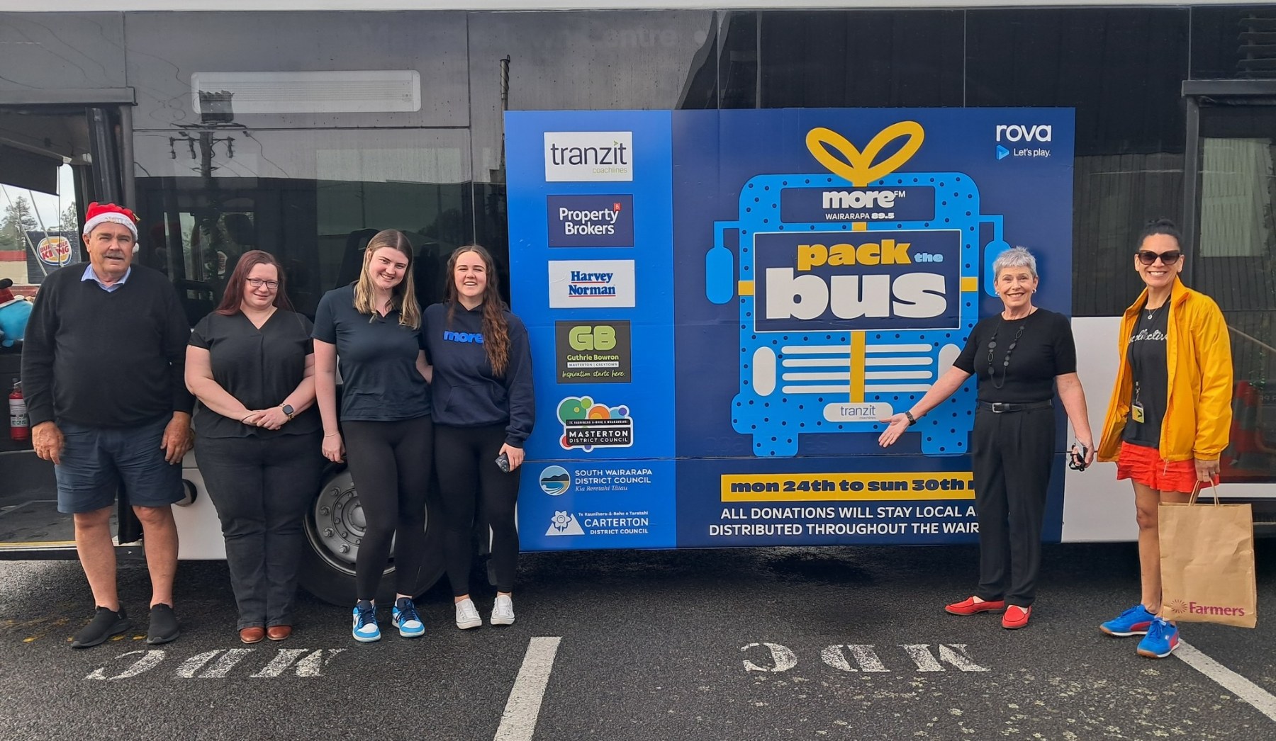 Six people stand in front of the 'Pack the Bus' bus